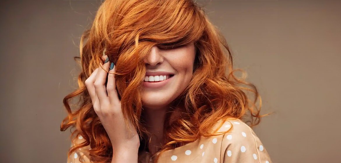 Frau mit orangenen Haaren fasst sich in ihr Haar